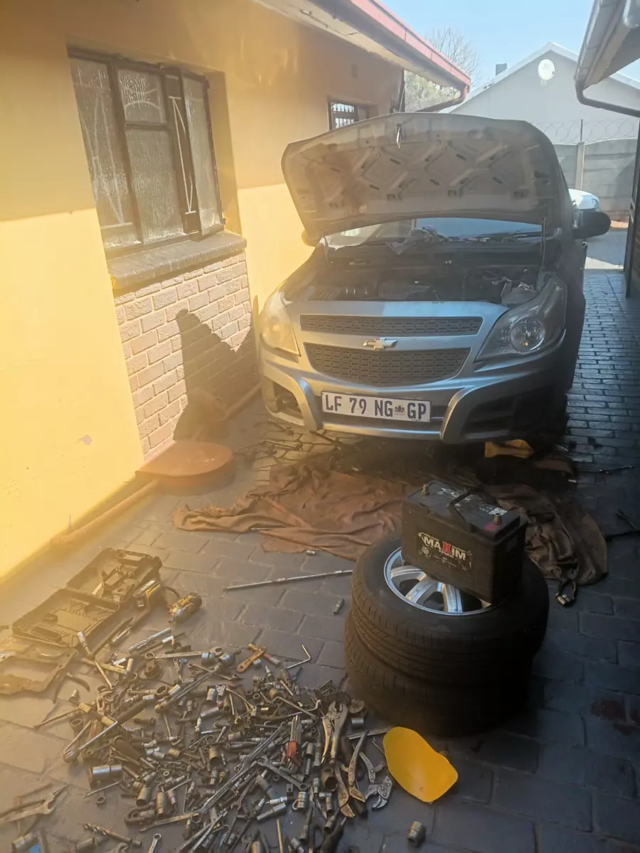 Silver car undergoing maintenance in a narrow driveway with scattered tools