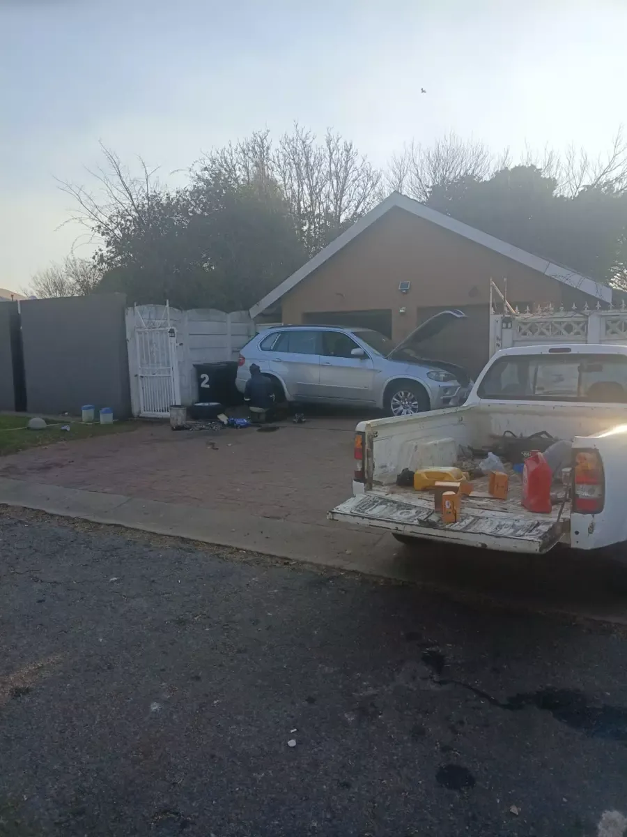 Mechanic working on a silver car in a driveway