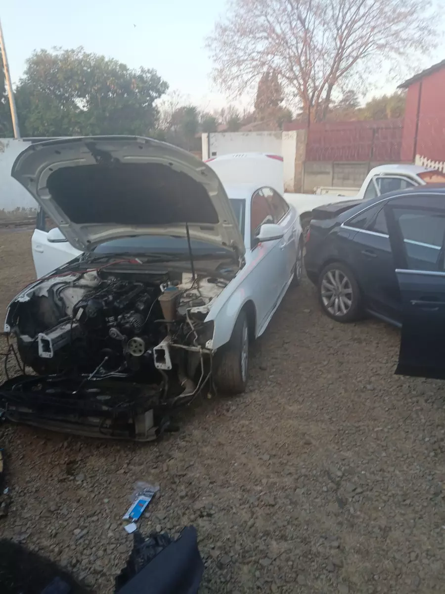 Dismantled white car being repaired in an outdoor gravel yard