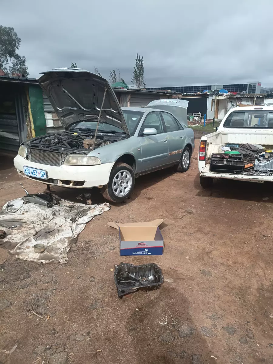 Silver car undergoing engine repair outdoors with open hood